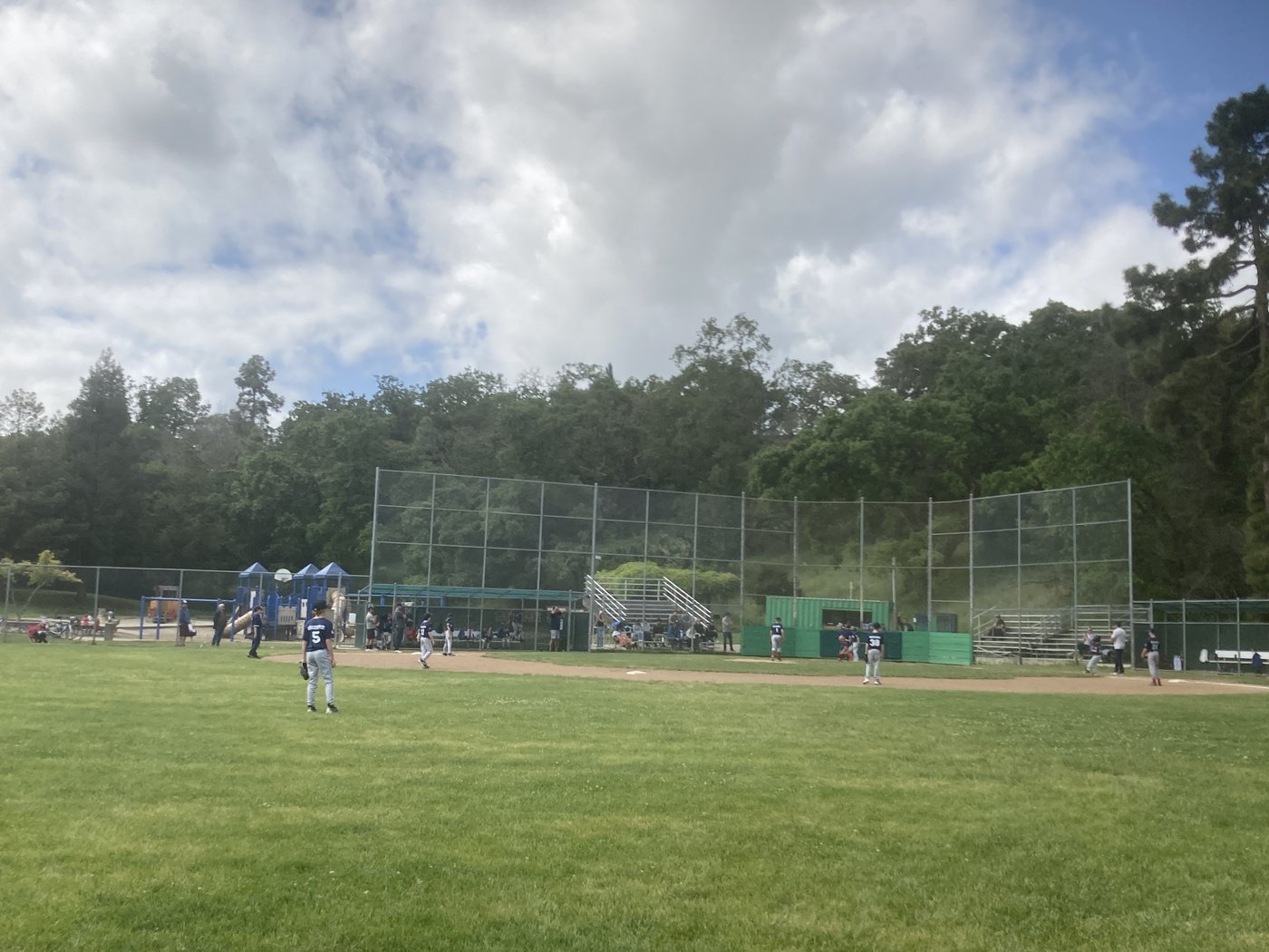 Things baseball parents say — youth baseball game in progress with bleachers behind the backstop