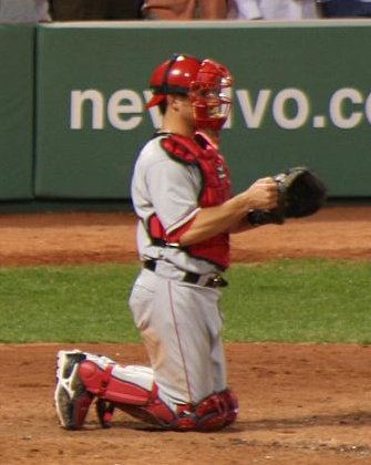 Catcher kneeling behind the plate in full gear with helmet, chest protector and leg guards