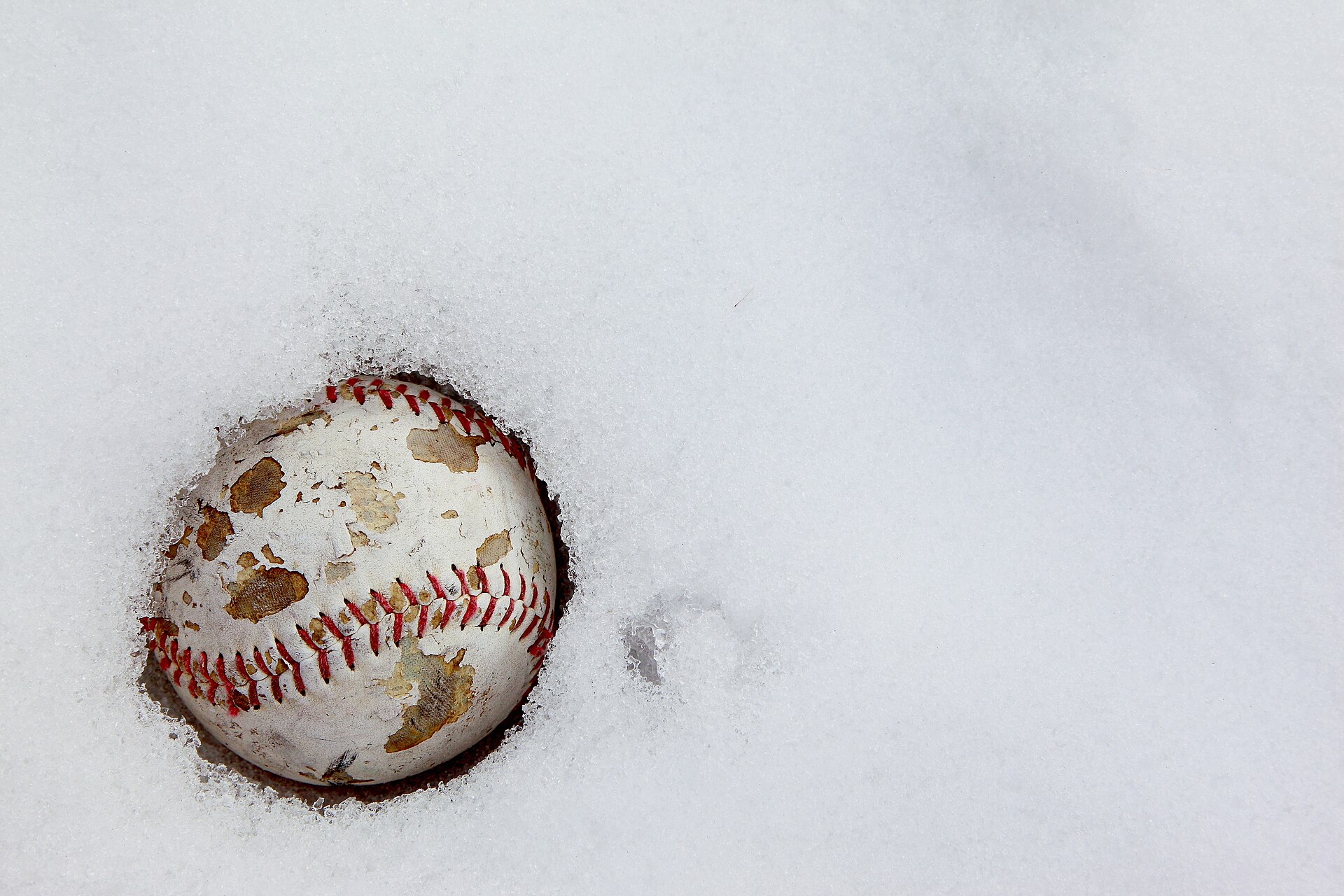Baseball sitting in snow, a reminder that cold weather baseball gear matters on winter game days