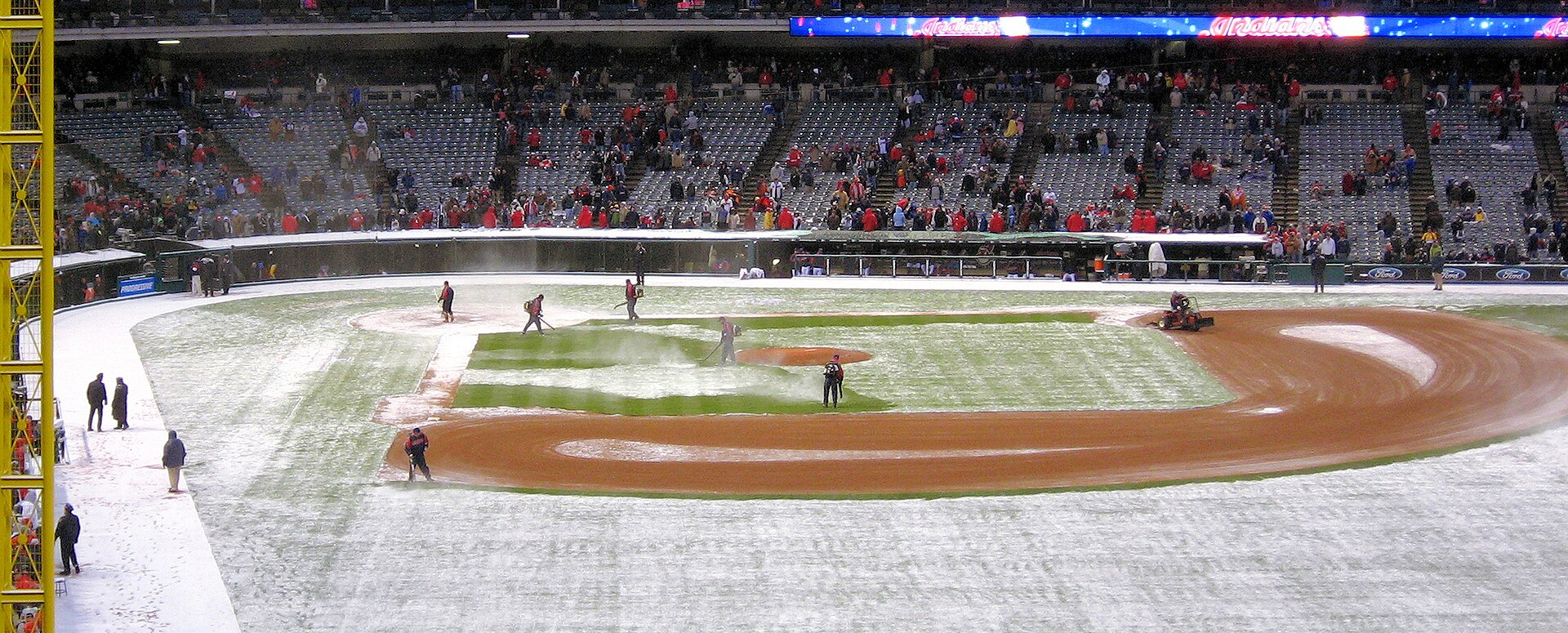 Grounds crew clearing a snow-covered baseball field during an early-season snow delay