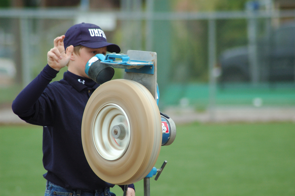 Coach loading a baseball into a wheel-style pitching machine, the type of machine used in many indoor baseball training facilities