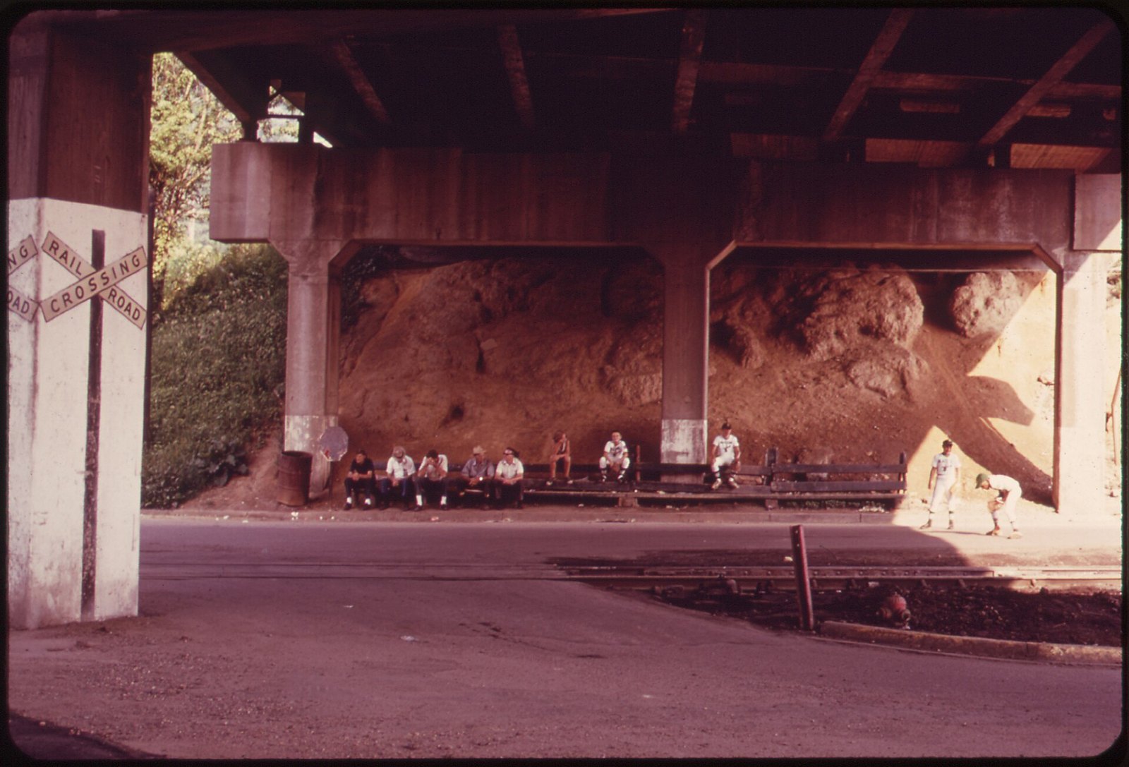 Little League players sitting on a bench under the Route 60 highway overpass in West Virginia in 1973