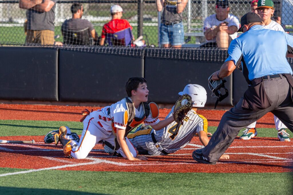 Youth catcher tagging a sliding runner at home plate as the umpire watches during a travel baseball tournament game on a turf field