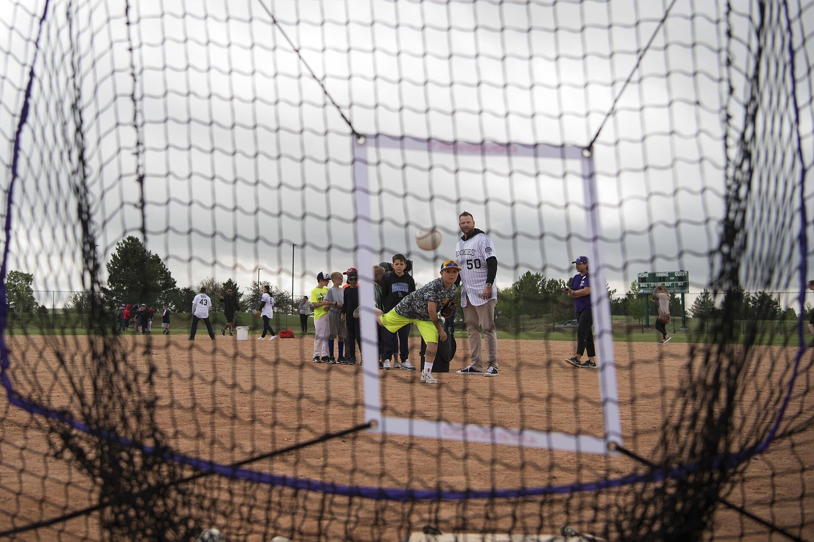 Colorado Rockies pitcher Brooks Pounders watches a young player pitch into a net at a youth clinic