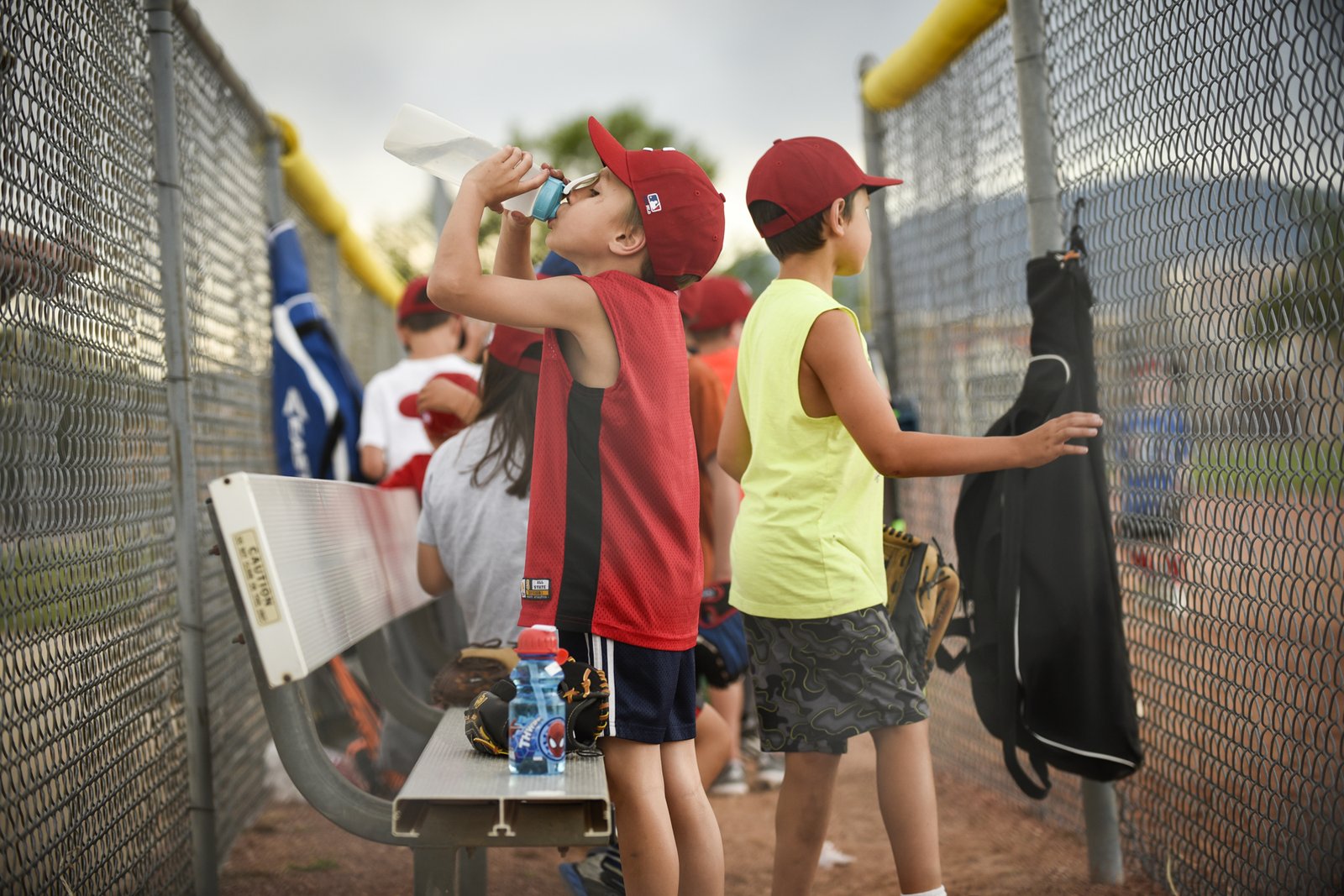 Youth baseball players drinking water at the dugout fence between drills, a moment to ask whether to switch select baseball teams