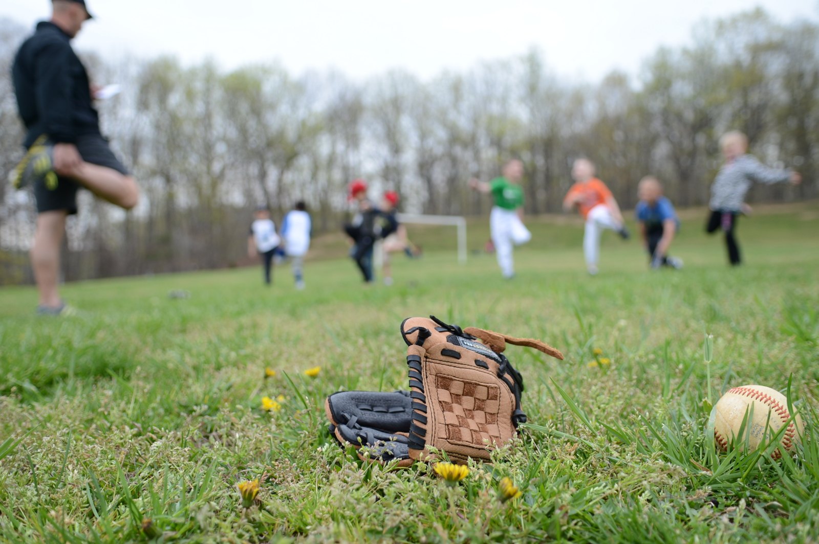 Baseball glove and ball resting in the grass while a youth team warms up at practice