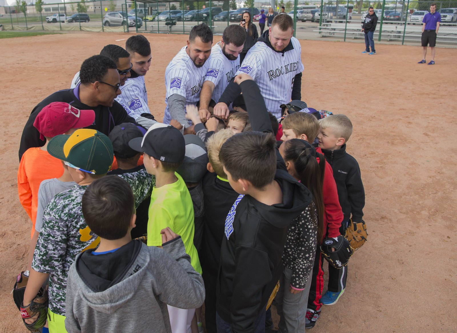 Young baseball players and coaches stacking hands in a huddle on a dirt infield before practice