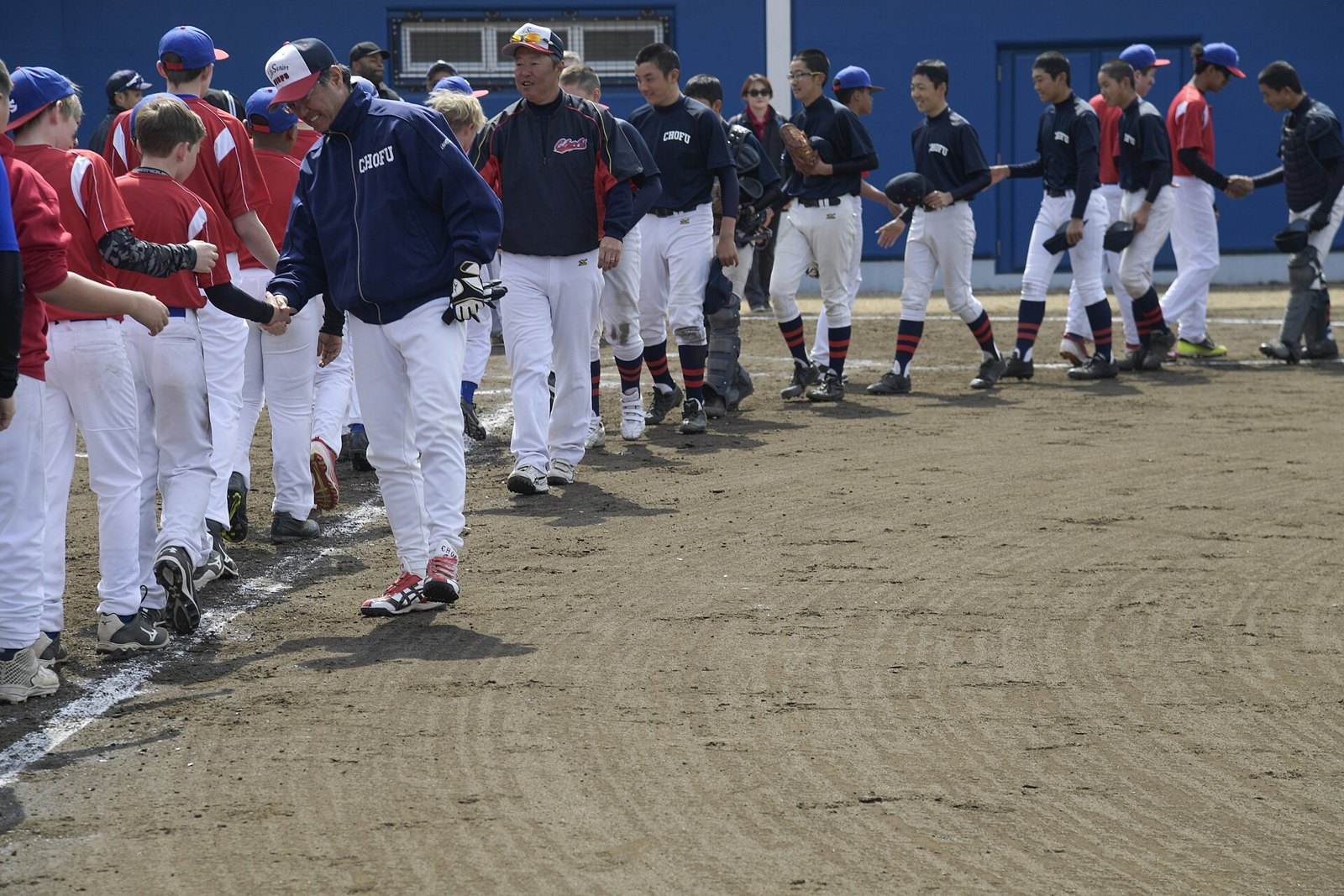 Two youth baseball teams in red and navy uniforms shaking hands in a line after a game